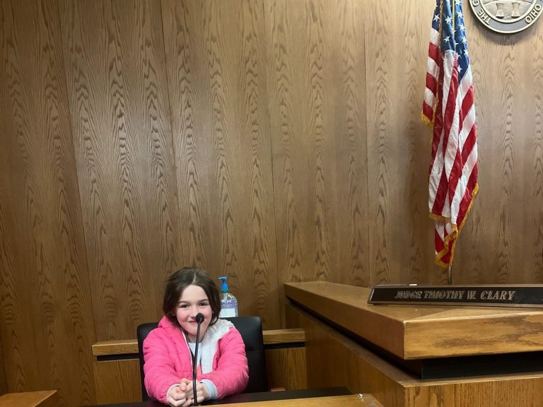 A visitor seated at a microphone beside the judge’s bench